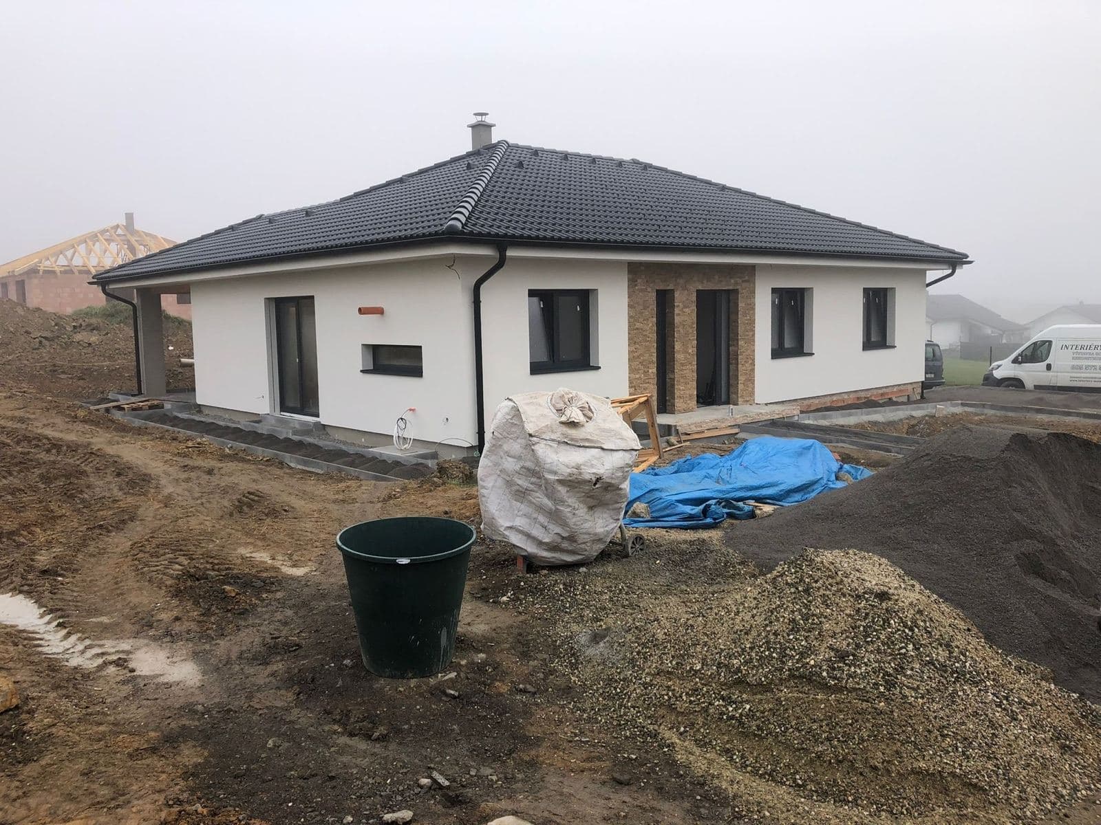 Dokončovaná fasáda bungalovu s antracitovými okny a kamenným obkladem u vstupu