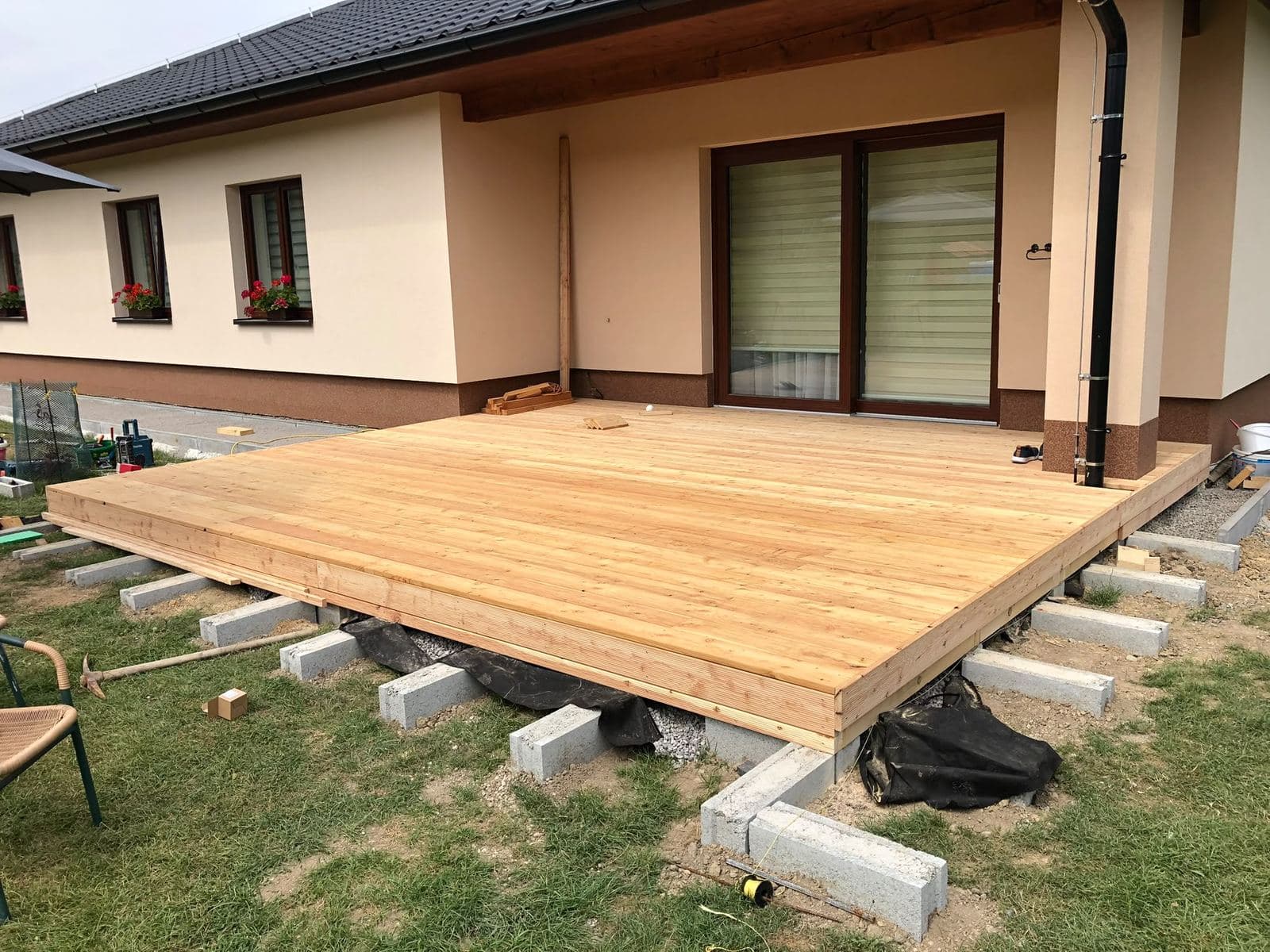 Nová modřínová terasa na betonových patkách před posuvnými dveřmi bungalovu